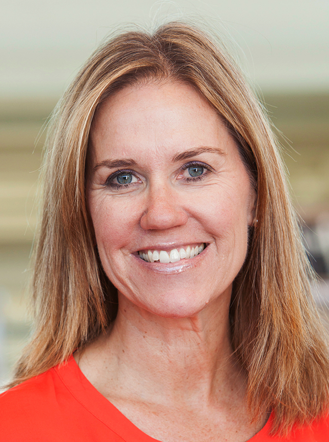 Light-skinned woman in red v-neck sweater, with blonde hair and blue eyes, smiling to the camera