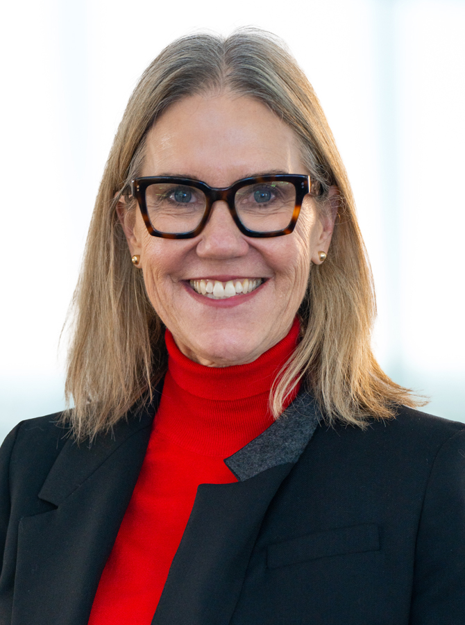 Light-skinned woman in red turtleneck sweater, with blonde hair and blue eyes, smiling to the camera