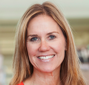 Light-skinned woman in red v-neck sweater, with blonde hair and blue eyes, smiling to the camera