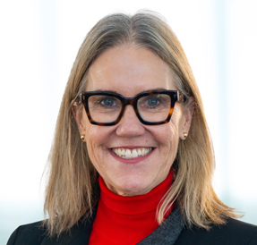 Light-skinned woman in red turtleneck sweater, with blonde hair and blue eyes, smiling to the camera